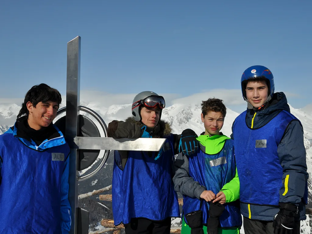 Gruppe posiert am Gipfelkreuz gegen den blauen Himmel.